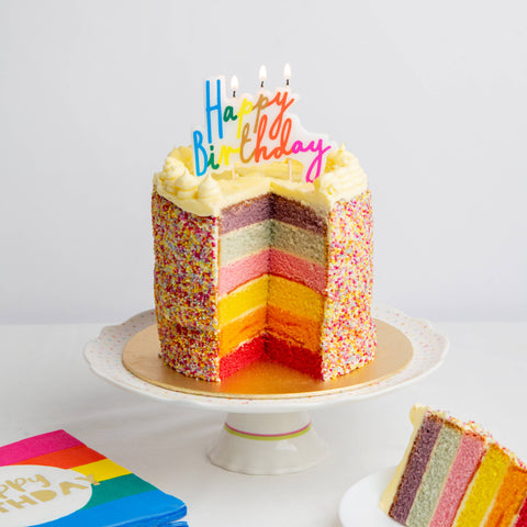 Colorful birthday cake with a slice taken out on a white plate, surrounded by colorful napkins.