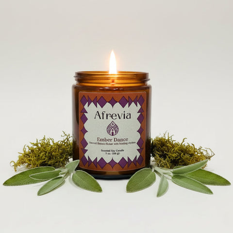 An amber glass jar candle labeled 'Afrevia Ember Dance' sits on a wooden table, with a large beige container in the background.