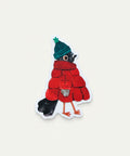 A die-cut sticker featuring a whimsical bird dressed in a red quilted winter coat, a green knit hat, and black boots, placed on a light wood grain surface.