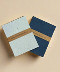 Two notebooks with denim accents on a cardboard surface with Vistaprint branding.
