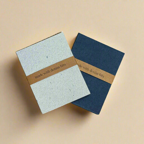 Two notebooks with denim accents on a cardboard surface with Vistaprint branding.
