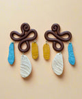 Pair of brown earrings with colorful hanging elements on a wooden surface
