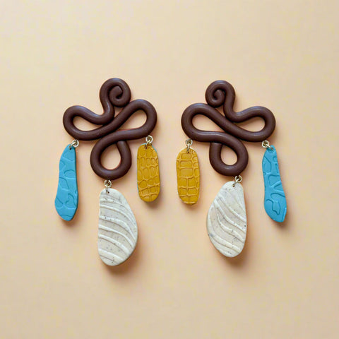 Pair of brown earrings with colorful hanging elements on a wooden surface