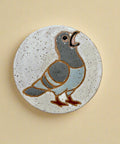 Round ceramic coaster with a pigeon design on a wooden surface