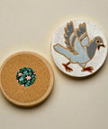 Two round coasters on a wooden surface, one with a cork back, the other with a bird illustration.