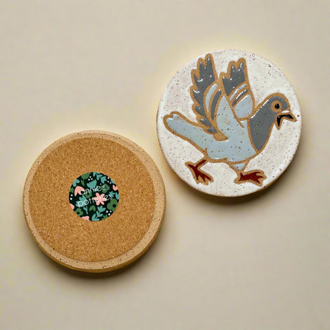 Two round coasters on a wooden surface, one with a cork back, the other with a bird illustration.