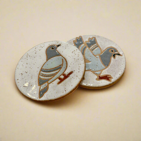 Two ceramic coasters with bird designs on a wooden surface