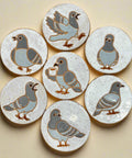 Set of ceramic coasters with pigeon designs on a wooden surface
