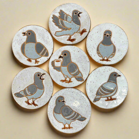 Set of ceramic coasters with pigeon designs on a wooden surface