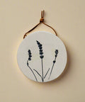 Round ceramic tile with lavender design hanging on a wooden surface