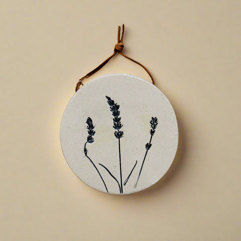 Round ceramic tile with lavender design hanging on a wooden surface