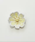 A small ceramic flower-shaped dish or jewelry stand with pale yellow and white petals and a gold-toned center, placed on a light wood surface.