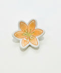 A small flower-shaped ceramic dish or trinket holder with orange petals, a white border, and a gold-toned center, placed on a light wood surface.