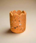Terracotta-colored candle holder with speckled pattern on a cardboard surface