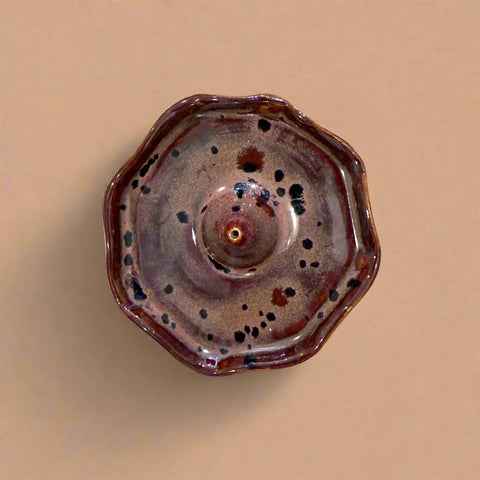 Brown ceramic incense holder with speckled pattern on a wooden surface