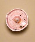 Pink ceramic incense holder with speckles on a wooden surface