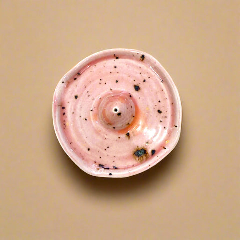 Pink ceramic incense holder with speckles on a wooden surface