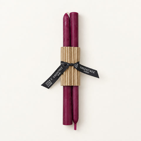 Two dark purple candles wrapped in a brown corrugated paper sleeve and tied with a black ribbon printed with the brand name 'The Entree', placed on a light wood background.