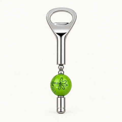 A novelty bottle opener with a polished silver metal body and a bright green spherical charm featuring a black line-art flower design, shown on a light wood grain background.