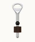 A bottle opener keychain with a polished silver metal finish, a dark green beaded accent, and a square dark brown wooden charm, displayed on a light wood grain surface.