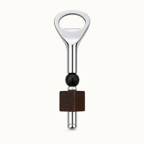 A bottle opener keychain with a polished silver metal finish, a dark green beaded accent, and a square dark brown wooden charm, displayed on a light wood grain surface.
