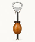 A bottle opener with a polished silver metal body and a round wooden handle, resting on a light brown wooden tabletop.