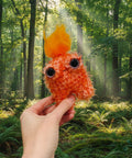 Hand holding a fluffy orange creature toy with a yellow top against a green park background