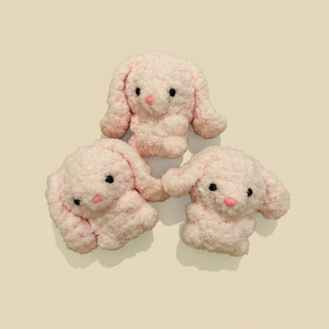 Three pink plush bunny toys on a wooden surface