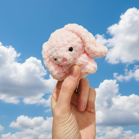 Small pink plush toy held in a hand against a neutral background