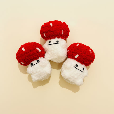 Three crochet mushrooms with red caps and white bodies on a wooden surface