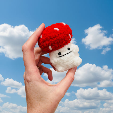 Hand holding a small plush toy with a red cap and white body against a plain background