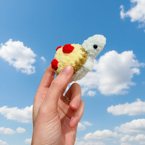 Hand holding a small crochet turtle toy against a plain background