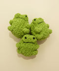 Three green plush frogs on a wooden surface