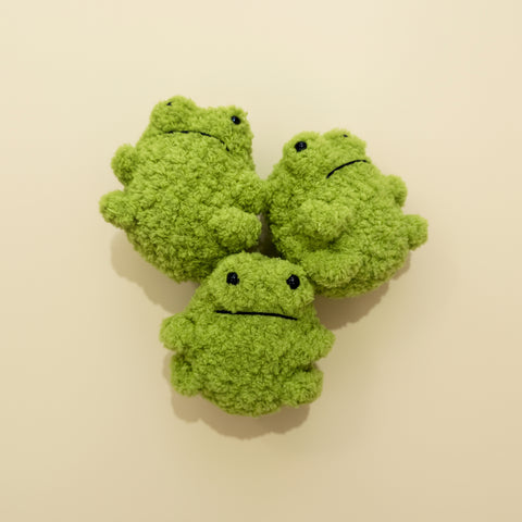 Three green plush frogs on a wooden surface