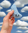 Hand holding a blue crocheted cloud with a face against a neutral background