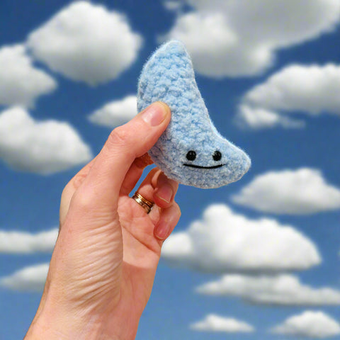 Hand holding a blue crocheted cloud with a face against a neutral background