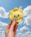 Hand holding a yellow plush sun toy against a plain background