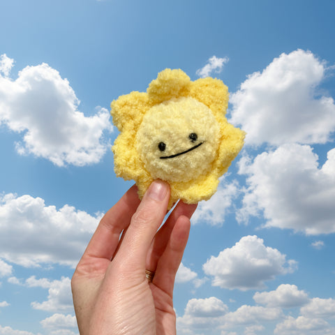 Hand holding a yellow plush sun toy against a plain background