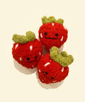Three red strawberry plush toys with green stems on a plain surface