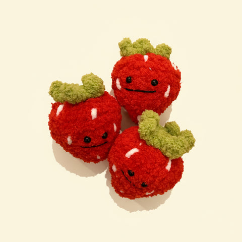 Three red strawberry plush toys with green stems on a plain surface