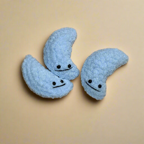 Three blue moon-shaped plush toys with faces on a wooden floor.