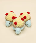 Three small plush toys resembling tortoises with red spots on a wooden surface.