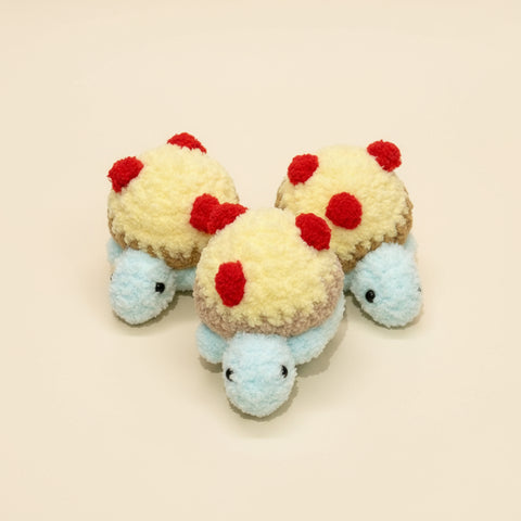 Three small plush toys resembling tortoises with red spots on a wooden surface.