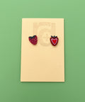 Strawberry-shaped earrings on a beige card with a wooden surface background