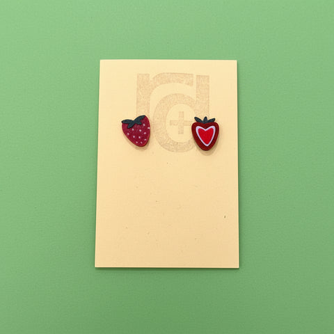 Strawberry-shaped earrings on a beige card with a wooden surface background