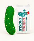 A green felt pickle-shaped item with yellow felt cplets and white stitching, placed next to a white paper bag printed with a cartoon pickle and the word 'PICKLE' on a light wood surface.