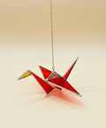 Red stained glass origami crane hanging on a chain against a blurred indoor background