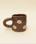 Brown ceramic mug with cartoon faces on a wooden surface