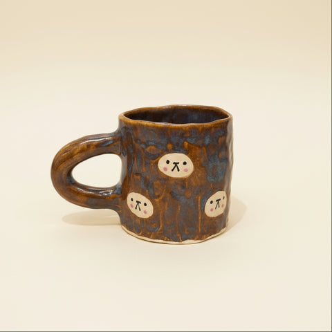 Brown ceramic mug with cartoon faces on a wooden surface