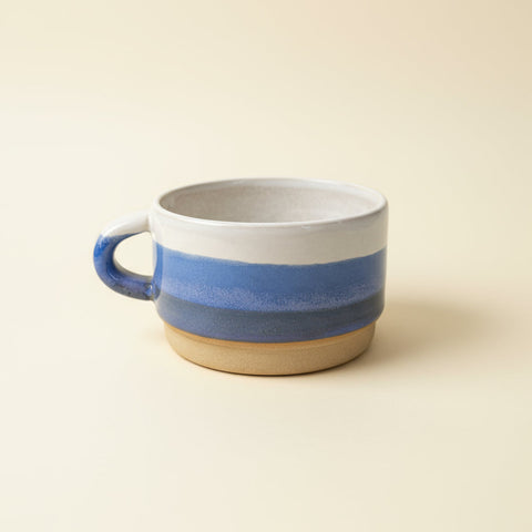 Ceramic mug with blue and beige stripes on a white surface